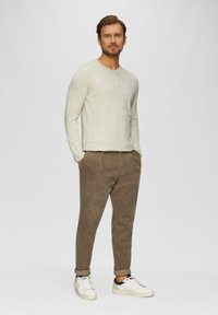Helle beigefarbene Langarmbluse mit rundem Ausschnitt, kombiniert mit braunen Cordhosen und weißen Sneakers. Einfaches Design, lässiger Schnitt.