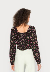 Blusa preta com flores, mangas longas bufantes, apresentando pequenas flores rosas e verdes, um decote quadrado nas costas e detalhes franzidos.