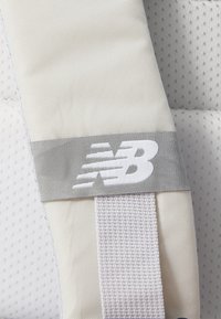 New Balance-logoen på et teksturert hvitt stoffrem med et grått aksentbånd. Remmen har et vevd design med subtile hevede mønstre.