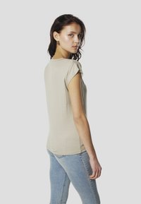 Beež lühikeste varrukatega pluus ümmarguse kaelusega ja peene läikega. Sile tekstuur, lihtne disain ja lõdvestunud lõige. Kaasas hele sinised teksad.