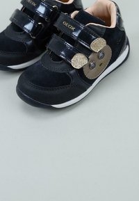 Zapatillas infantiles de ante negro y sintético brillante con dobles correas de Velcro, diseño de cara de mono y suelas de goma blanca.