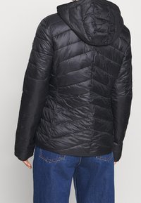 Veste matelassée noire avec une capuche, présentant des coutures en chevrons et une texture lisse. Le dos affiche un design élégant et ajusté.