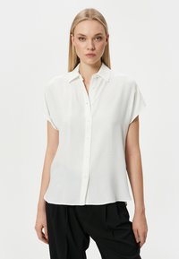 Camisa blanca de manga corta con botones en la parte delantera, fabricada en una tela suave y con un corte relajado. El cuello es clásico, con una textura suave y sin patrones.