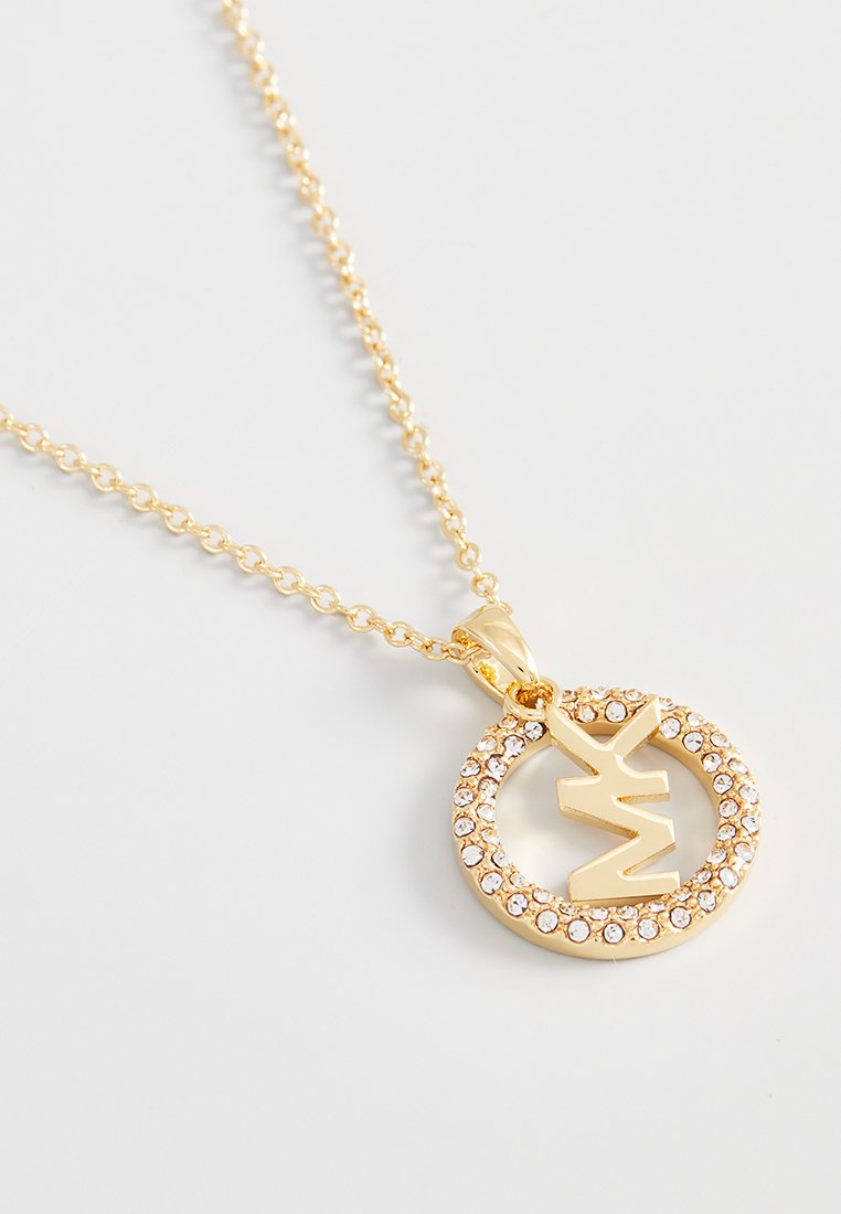 Collana d'oro con un pendente rotondo, caratterizzato da una lettera stilizzata e circondato da piccoli strass trasparenti. La catena è delicata e a maglie.