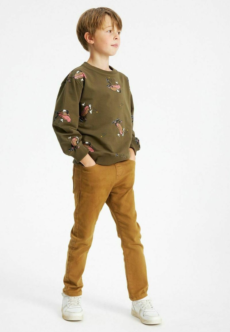 Olivgrön sweatshirt med lekfulla djurtryck, i kombination med slim-fit bruna byxor. Vita sneakers fulländar den avslappnade stilen.