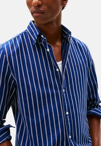 Camisa de manga larga azul marino con rayas blancas verticales y un pequeño logo en el pecho. La tela parece ligera y con textura.