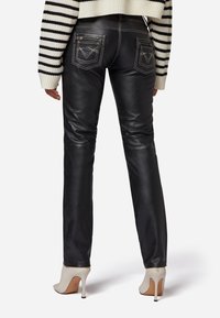 Zwarte leren broeken met een slim fit, gedetailleerde achterzakken, contrasterende stiksels en gecombineerd met beige hoge hakken.