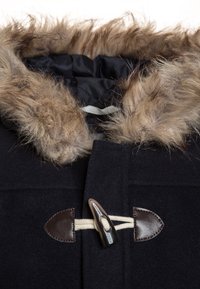 Cappotto nero con cappuccio, caratterizzato da un bordo in pelliccia sintetica color beige, chiusure a bottone e un'esterno in lana testurizzata. Include dettagli in corda crema.