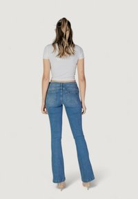 Jeans flare in denim azzurro chiaro con vita alta, dotati di due tasche posteriori e un logo ricamato discreto, abbinati a un top bianco aderente.