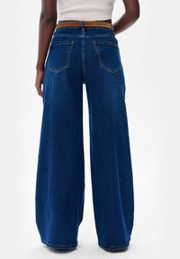Spodnie dżinsowe z szerokimi nogawkami w kolorze niebieskim, o wysokim stanie, z brązowym pasem, dwiema tylne kieszeniami i gładką fakturą.
