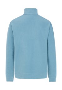 Šviesiai mėlynas pūkinis džemperis su aukštu apykakle, ilgomis rankovėmis ir lygiu, minkštu paviršiumi. Pasižymi minimalistiniu dizainu ir matomų detalių stoka.