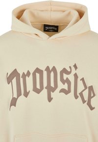 Vaaleancreme värinen huppari, jossa on suuri ruskea goottityylinen "Dropsize" logo rinnassa. Hupparissa on etutasku ja säädettävä narukkopäällyste.