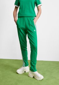 Green athletic pants with white side stripes and an elastic waistband, paired with a green short-sleeve top. Chunky white sneakers.