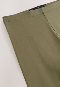 Khaki stretchleggings i et glat, mat stof. Har en flad linning og en slank pasform, velegnet til afslappet eller aktivt brug.