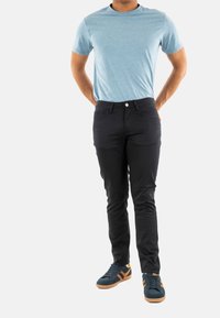 T-shirt bleu clair à manches courtes, pantalon noir ajusté avec poches avant, et baskets noires avec des rayures orange et semelles en caoutchouc.
