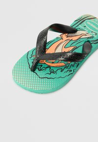 Black rubber flip-flop with textured straps over a turquoise footbed featuring a printed design with a cartoon character and dot pattern.