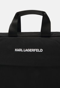 Svart stoffpose med sterke håndtak, med hvit brodert "KARL LAGERFELD"-logo. Glatt tekstur, rektangulær form, minimalistisk design.