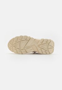 Light beige shoe sole with rugged tread design, featuring thick rubber texture and multi-directional grooves for traction.