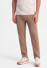 Beige Baumwollhose mit Slim-Fit und subtiler Textur, kombiniert mit hellen Sneakern, die eine Mischung aus beige und weißen Akzenten aufweisen.