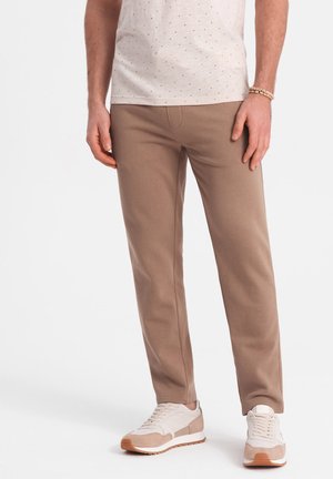 Pantalones de algodón beige con un corte slim y una textura sutil, combinados con zapatillas ligeras que presentan una mezcla de acentos beige y blancos.
