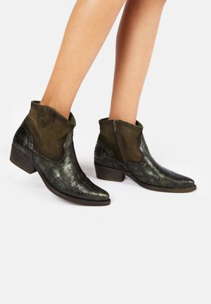 Bottines en cuir texturé crocodile vert avec un bout légèrement pointu, des accents en suede olive et une fermeture éclair sur le côté. Design à talon block.
