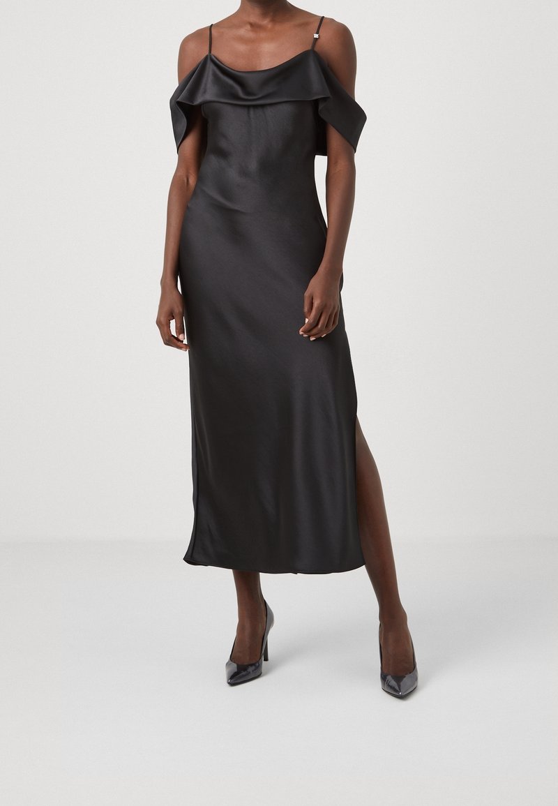 Svart satin slipklänning med off-shoulder volangdetalj, tunna axelband och en sidoflis, i kombination med svarta heels med spetsig tå.