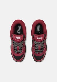 Sneakers rossi e neri con tomaia in tessuto texturizzato, lacci decorati e colletto imbottito con un logo sulla linguetta.