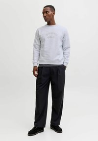 Lichtgrijze sweatshirt met reliëf "ORIGINALS"-tekst, gecombineerd met losse zwarte broek en zwarte schoenen, met een gladde stoftextuur.