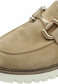 Beige suède loafer met een gestructureerd oppervlak, voorzien van een goudkleurige gesp en een witte rubberen zool. Ronde neus met decoratieve stiksels.