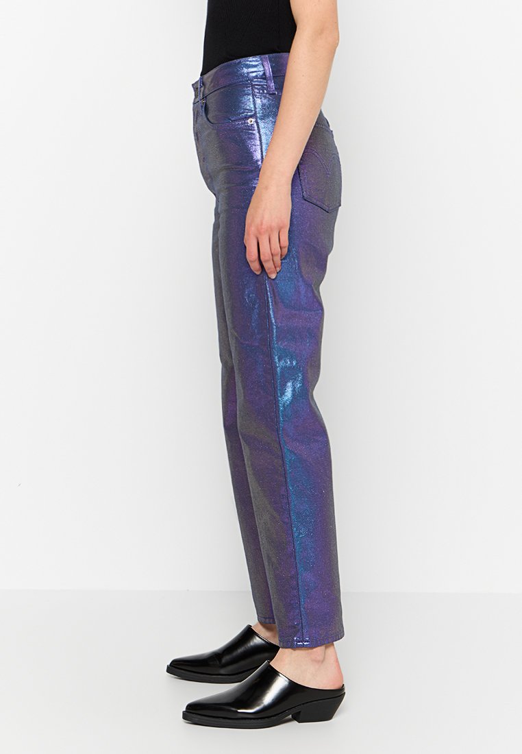 Jeans morados metálicos brillantes con pierna recta, que cuentan con bolsillos y un ligero brillo. Combinados con zapatos negros de lona brillantes y sin cordones.