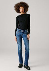 Melna garroku blūze ar laivas veida kakla izgriezumu, kopā ar zilām taisnām džinsām ar divu pogu aizdari un nelielu krokumu pie kabatām.