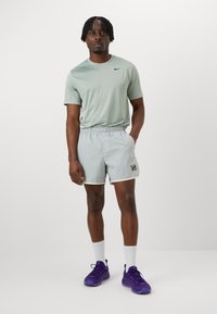 Svijetlosivi Nike majica, odgovarajuće kratke hlače s elastičnom gumom u struku i logotipom. Ljubičaste sportske cipele i bijele čarape upotpunjuju odjeću.