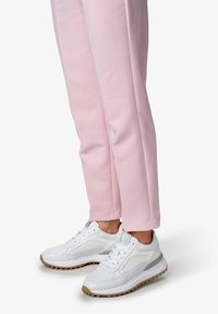 Baskets blanches en cuir texturé avec semelles en caoutchouc, associées à un pantalon tapered rose clair. Les chaussures présentent une accents gris et des lacets.