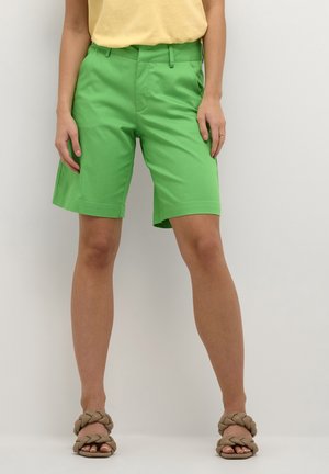Shorts en coton verts avec un devant plat, des poches latérales et des ourlets roulés. Associés à des sandales tressées brun clair. Texture lisse.