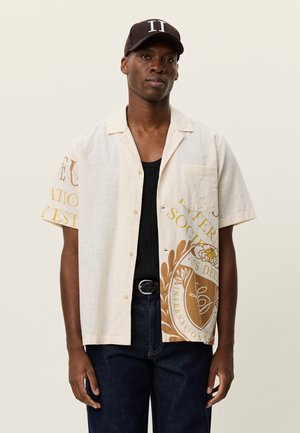 Kortærmet hørskjorte i creme med gul og brun grafisk print. Har en lomme og en løs pasform, kombinering med mørke jeans.