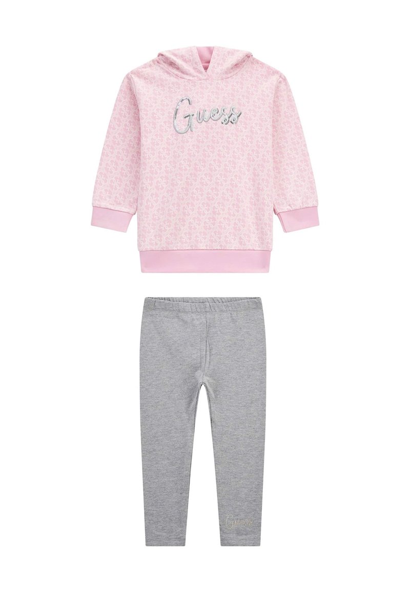 Rózsaszín kapucnis pulóver ismétlődő mintával és fényes betűkkel írt 'Guess', szürke leggings-szel párosítva, melyek alján hímzett 'Guess' felirat található.
