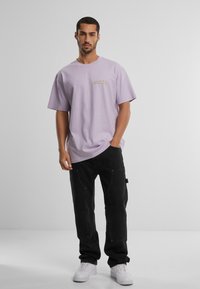 Lavendel bomuld t-shirt med korte ærmer og et lille logo på brystet, parret med sorte cargobukser og hvide sneakers.