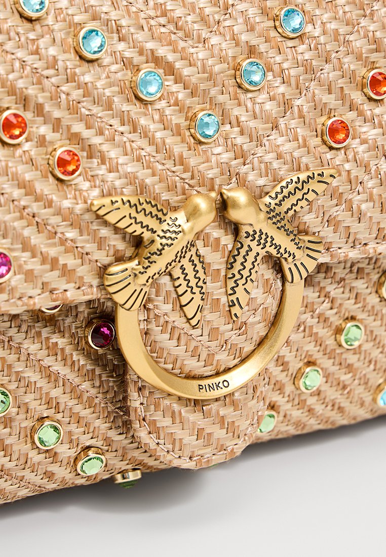 Bolso tejido beige que presenta gemas coloridas y un cierre de anillo en tono dorado adornado con dos pájaros estilizados. Superficie texturizada y detalles elaborados.
