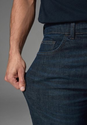 Donkerblauwe denim jeans met een klassieke vijf-pocketontwerp. De stof heeft een subtiele textuur en de tailleband is voorzien van een riemlus.