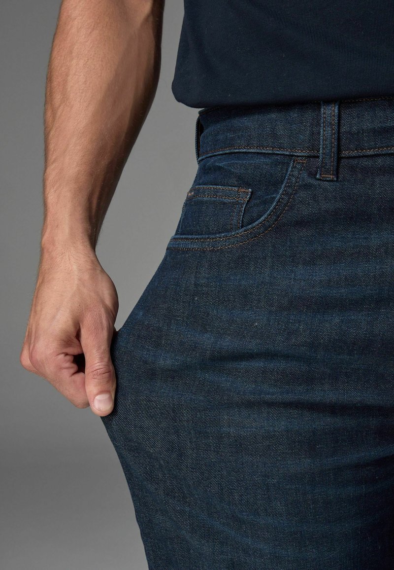 Tumedast sinine denim materjalist teksapüksid, mis omavad klassikalist viie tasku disaini. Kangas on kergelt tekstureeritud ning vöökoht sisaldab vööaasasid.