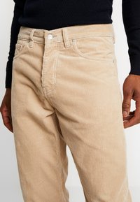Beige corduroy broek met verticale strepen, vijf-pocket ontwerp en metalen knoopsluiting, met een gestructureerde stof.