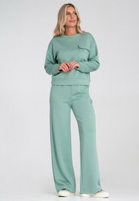 Jasnozielony zestaw odzieży domowej składający się z krótkiego swetra z długim rękawem z kieszonką na piersi oraz spodni o szerokich nogawkach, wykonany z miękkiego materiału.