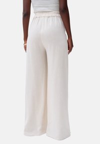 Lange, wijde broeken van lichtgewicht, gestructureerde witte stof met een elastische tailleband. Detail van de achterkant laat de vloeiende silhouet en schone zoomlijn zien.