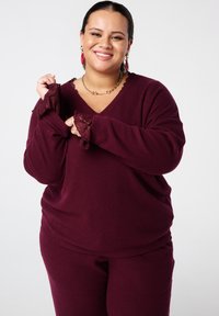 Ensemble de détente en maille côtelée bordeaux avec un haut en V et des manches évasées rehaussées de détails en dentelle, accompagné d'un pantalon ajusté assorti.