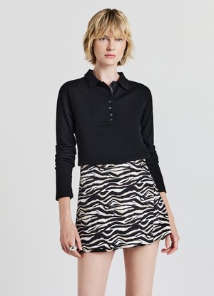 Schwarzes langärmeliges Poloshirt mit Knopfverschluss, kombiniert mit einem kurzen Rock mit auffälligem schwarz-beigem Zebra-Muster.