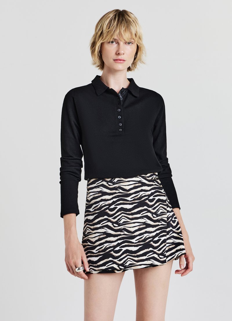 Polo shirt nero a maniche lunghe con placket abbottonato, abbinato a una gonna corta con un audace motivo a strisce zebra in nero e beige.