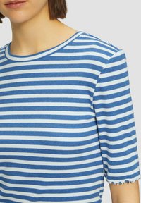Top de manga corta a rayas azul y blanco con cuello redondo, que presenta una textura acanalada y un dobladillo festoneado en las mangas.