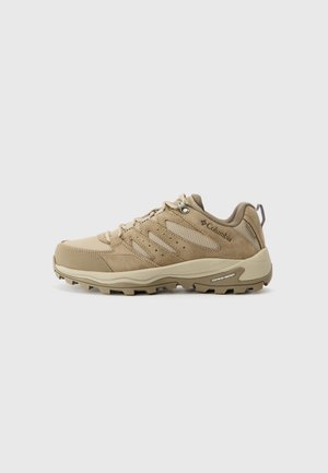 Beiger Columbia Wanderschuh mit Schnürsenkeln, Mesh-Akzenten, gepolstertem Kragen und robuster Sohle mit der Bezeichnung Omni-Grip auf hellem, einfarbigem Hintergrund.