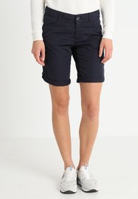 Shorts di cotone blu navy con risvolti, tasche frontali e chiusura a bottone, abbinati a scarpe da ginnastica grigie.