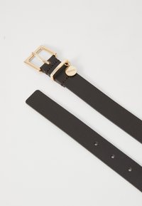 Cinturino in pelle marrone con fibbia dorata, dotato di un ciondolo rotondo inciso con la scritta "HUGO". Texture liscia e numerosi fori per la regolazione.